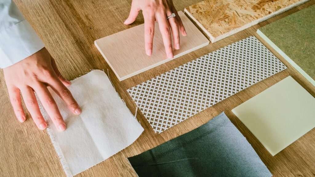 Person arranging assorted material samples on table.