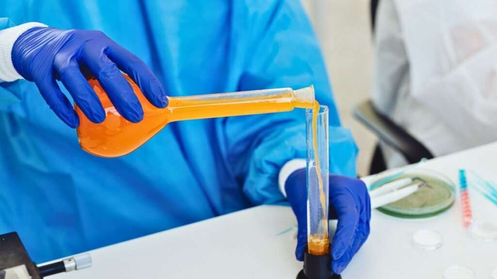 Scientist pouring orange liquid in laboratory flask